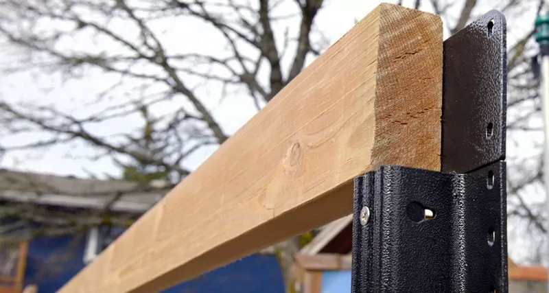 Image of a wooden rail on top of a lifetime steel post with trees in the background with fallen leaves to help illustrate Winter fence replacement fence post types
