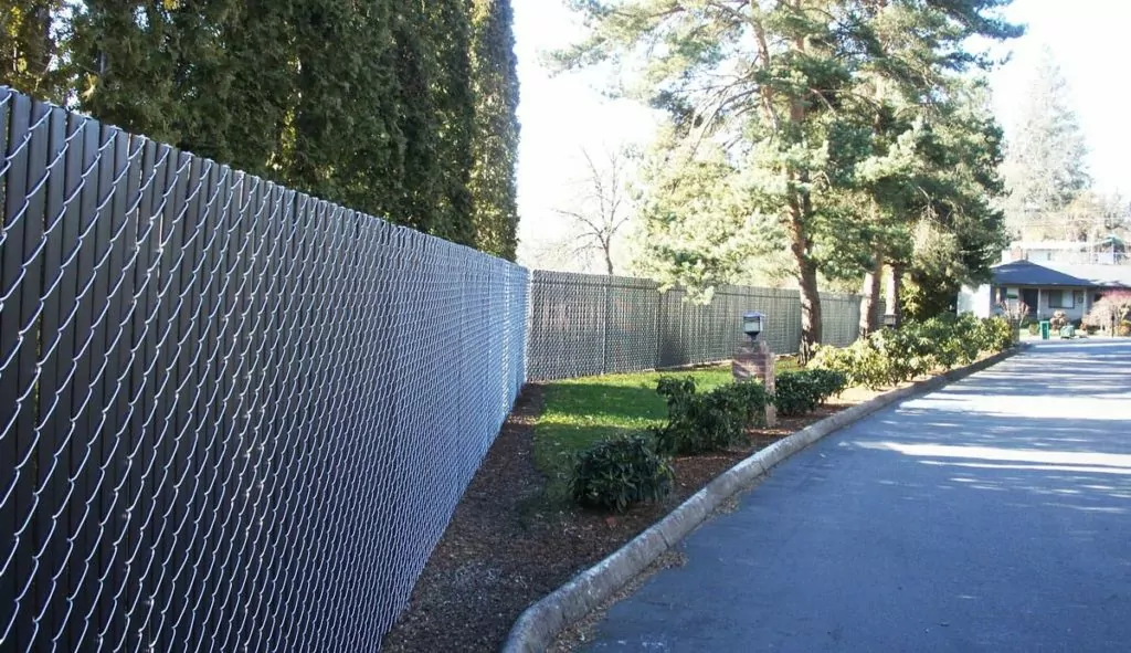 A long, chain link fence with slats for privacy alongside a residential property.