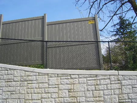 A vinyl fence on top of a retaining wall with a black chain link fence to illustrate fence ideas for corner house.