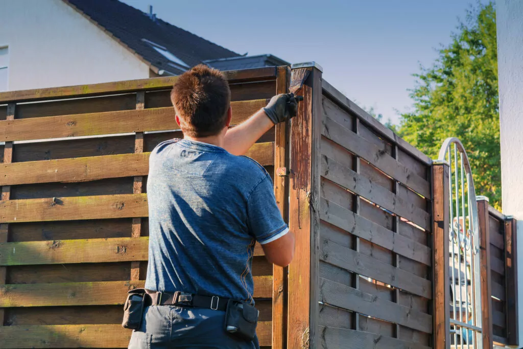Man staining a wood corner fence to illustrate fence ideas for corner house.